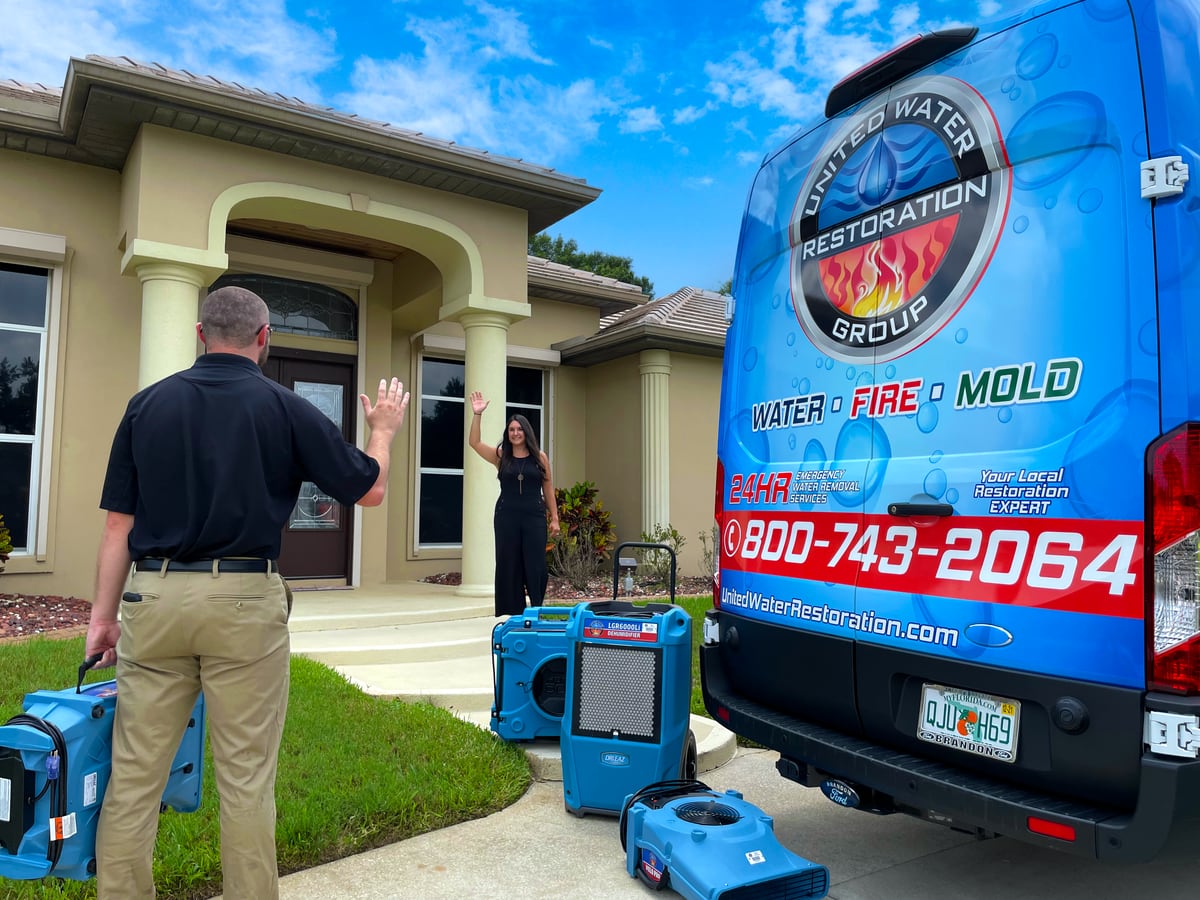 A technician carrying equipment back to the van, waving to the homeowner at her door